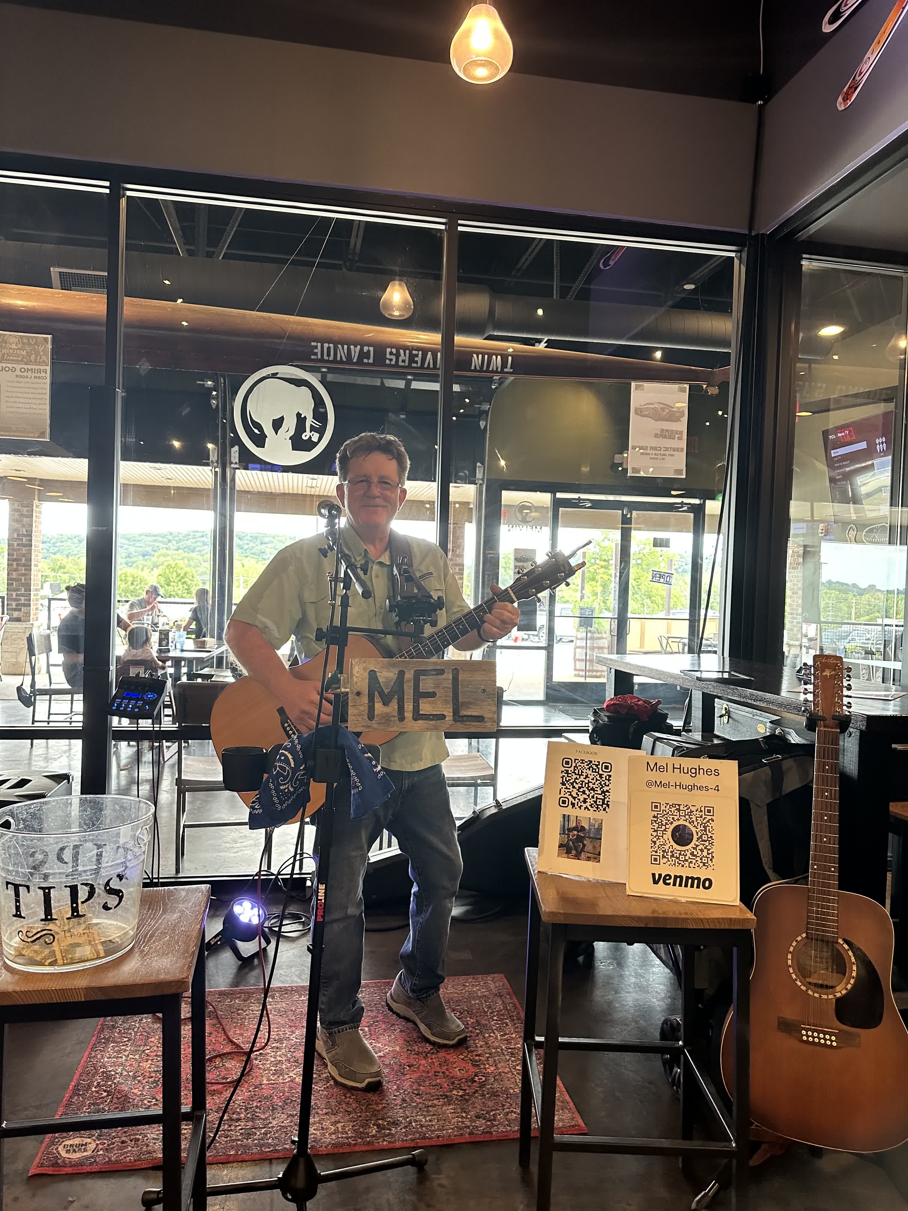 Mel Hughes performing indoors beneath the wooden MEL sign
